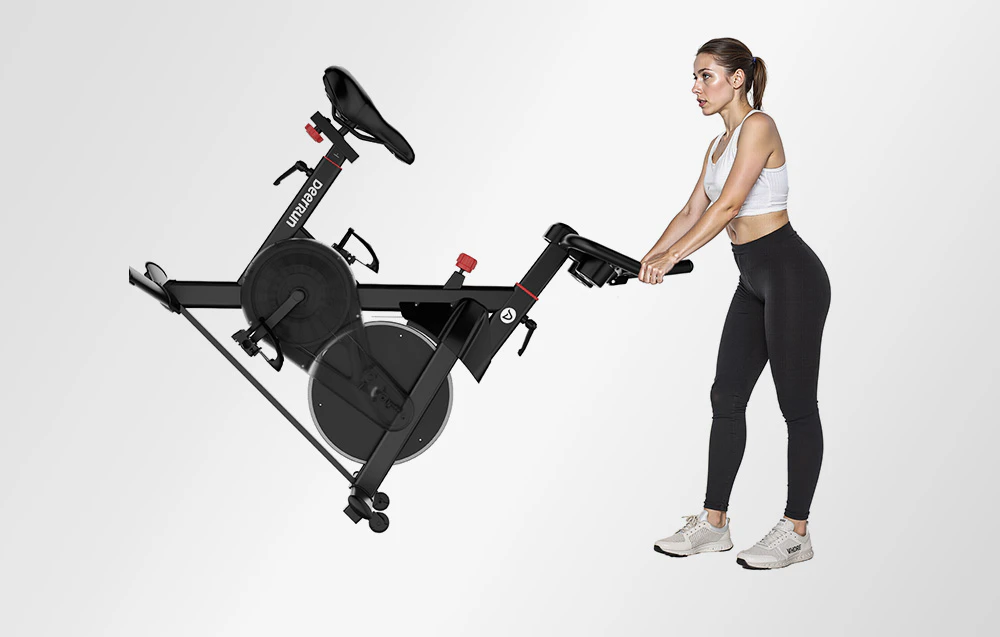 Femeie care înclină o bicicletă de exerciții neagră pentru depozitare sau transport pe un fundal deschis