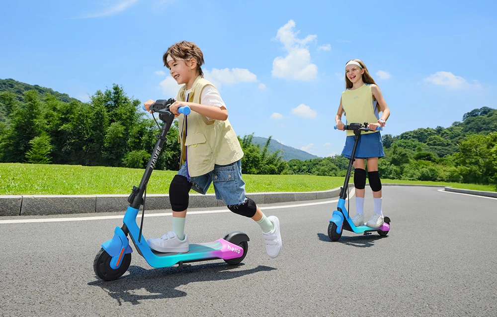 Doi copii se plimbă cu trotinete albastre pe un drum asfaltat, înconjurat de verdeață