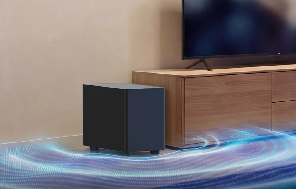 Un subwoofer wireless pe podea, lângă un suport de televizor