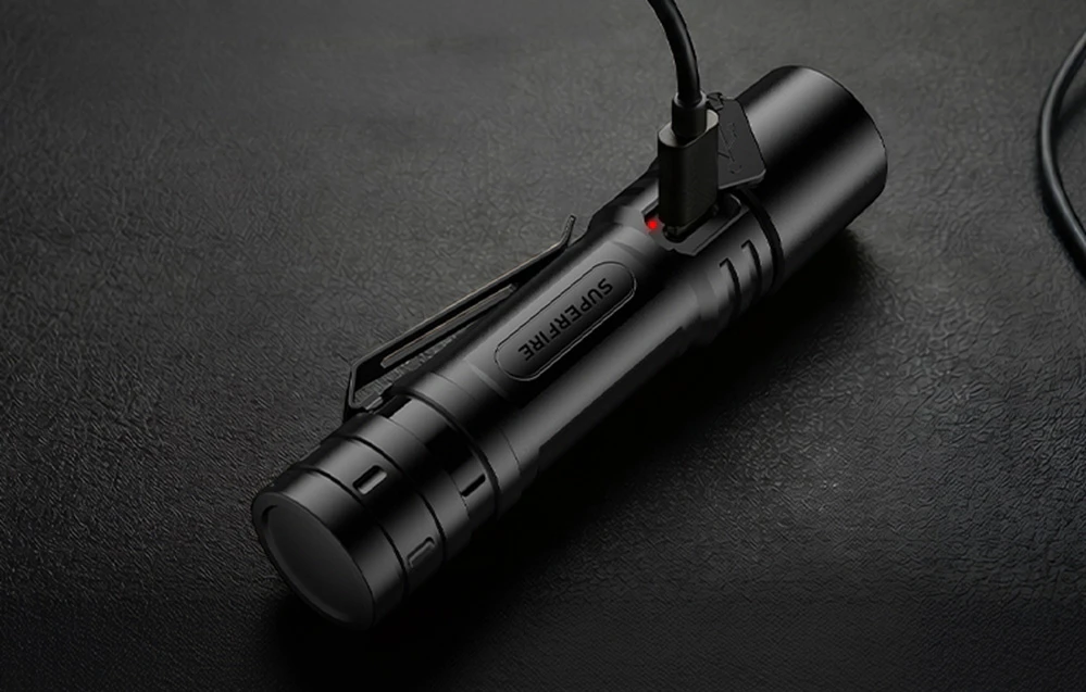 O lanternă portabilă Superfire neagră conectată la un cablu USB cu un LED roșu de încărcare
