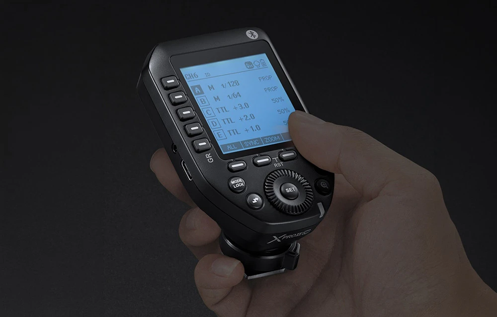 Declanșator radio negru Godox XProII cu ecran LCD retroiluminat, ținut în mână pe un fundal întunecat