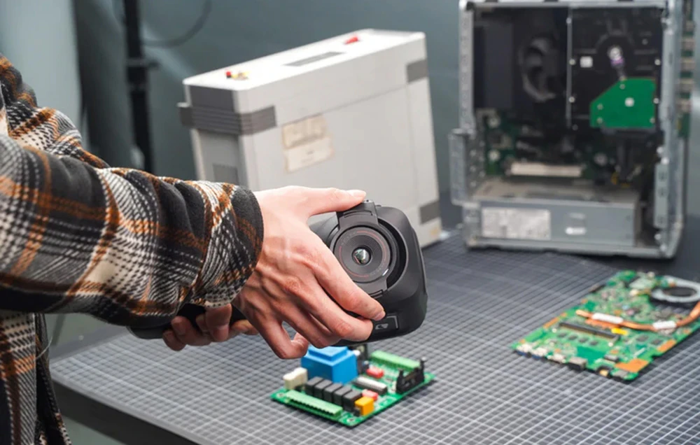 O mână ține o cameră termovizuală Thermal Master îndreptată spre componente electronice și carcasa deschisă a unui computer