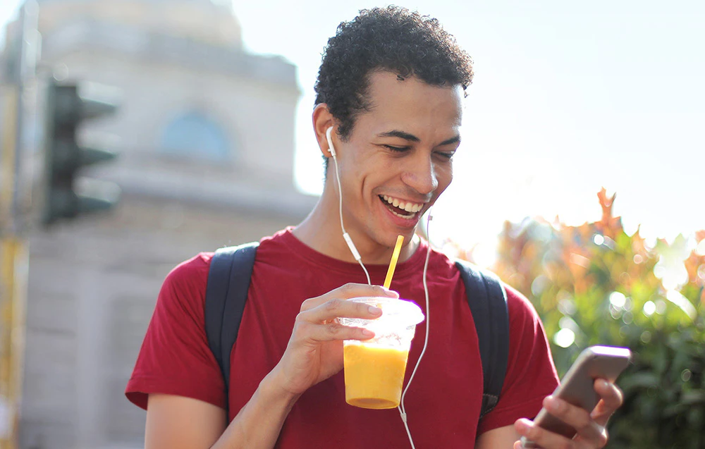 Un bărbat zâmbitor care ține un smartphone și un pahar cu suc