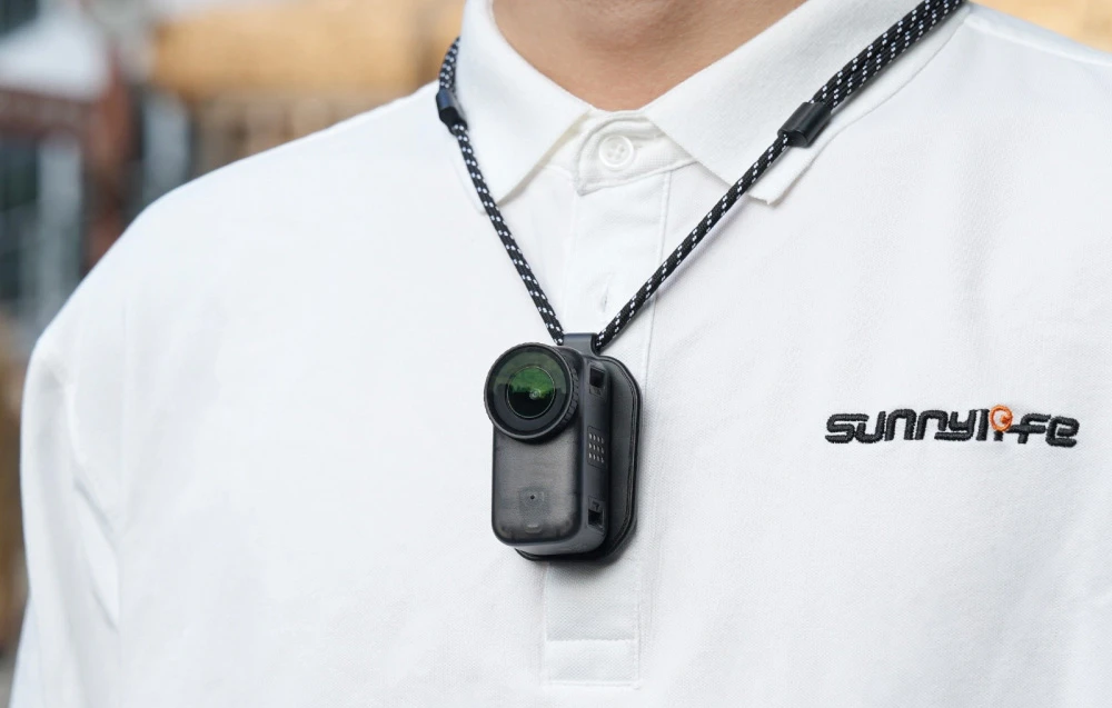 Un bărbat îmbrăcat într-un tricou polo alb, cu o cameră miniaturală neagră pe un suport magnetic atârnat la gât.