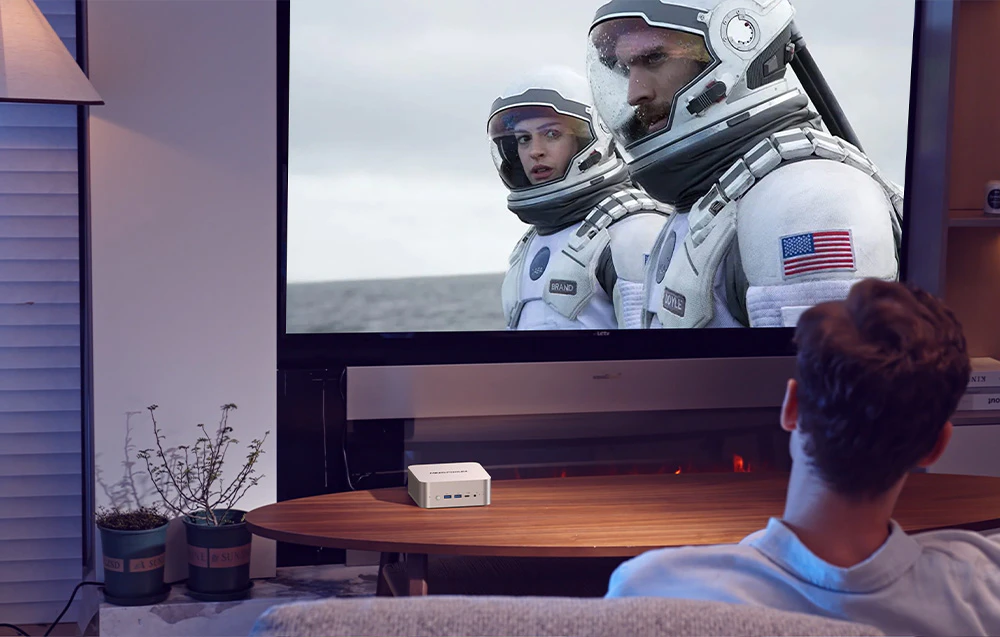 Un bărbat se uită la un film în timp ce stă pe canapea, pe masa de lângă mini pc