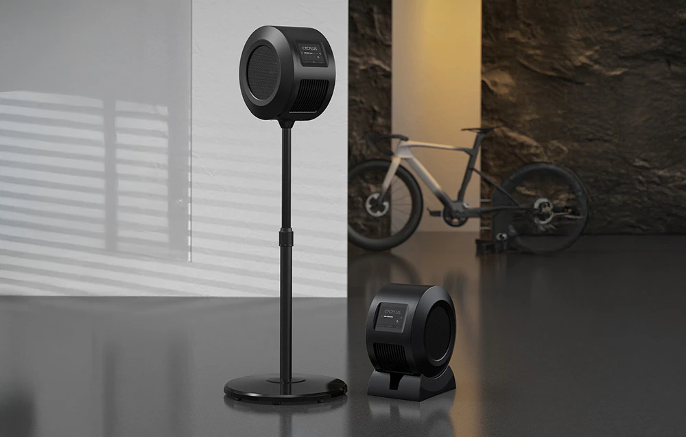 Două ventilatoare Cycplus negre pe un suport și o bază în camera cu bicicleta