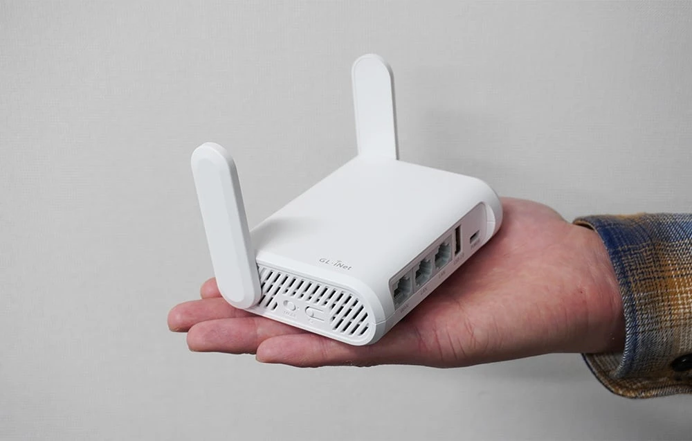 Un router GL.iNet alb ținut în palmă, pe un fundal gri