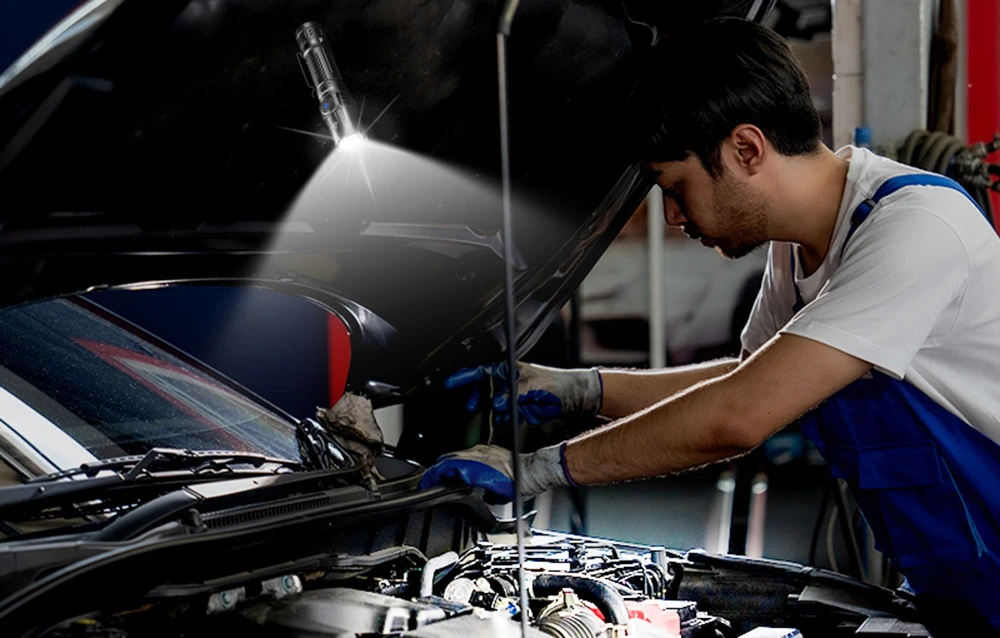 Mecanicul în costum albastru repară motorul mașinii folosind lanterna pentru iluminare