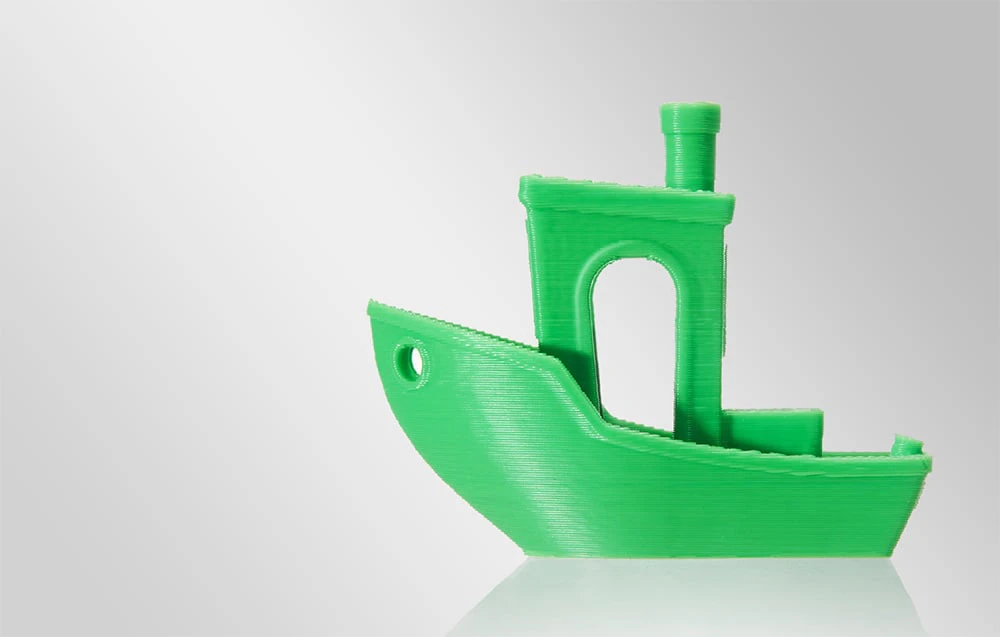 Un model de barcă verde imprimat pe o imprimantă 3D pe un fundal alb.
