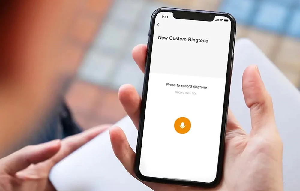 O mână ținând un smartphone cu ecranul „New Custom Ringtone” și un buton de microfon pentru înregistrarea audio
