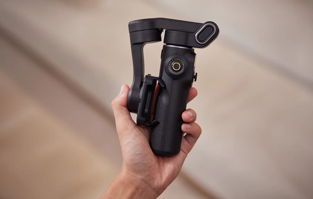 O mână care ține un gimbal pliat — o imagine a formei compacte a dispozitivului.