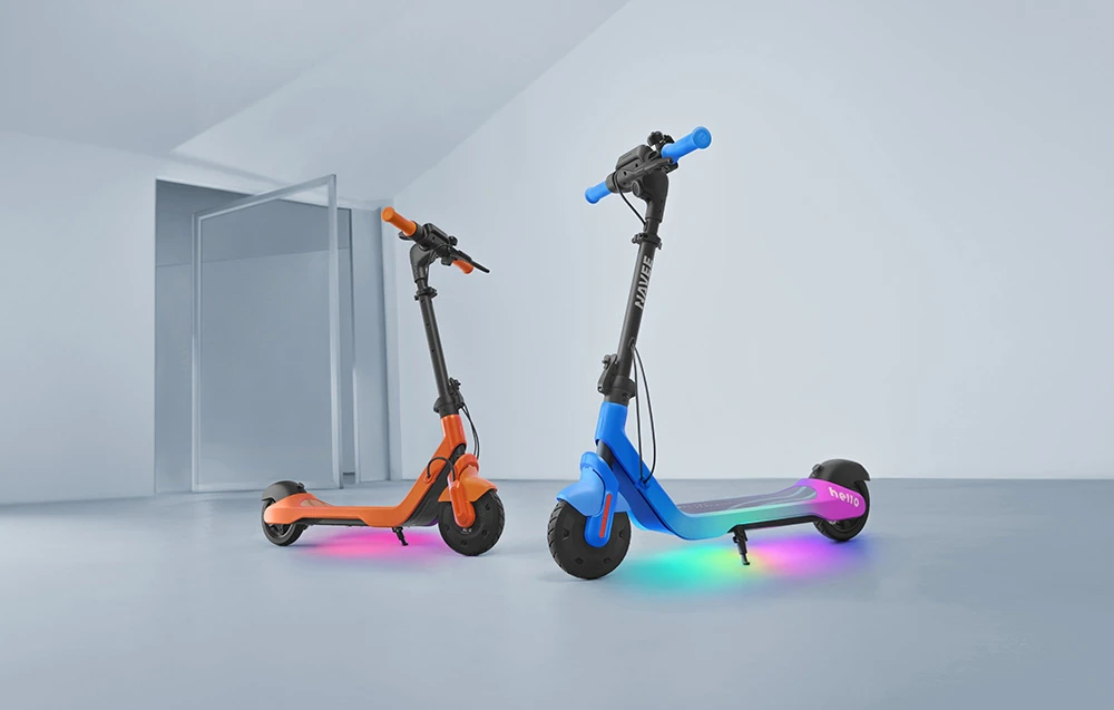 Două trotinete electrice pentru copii, de culoare albastră și portocalie, stau într-o cameră luminoasă, cu iluminare LED, sub o platformă
