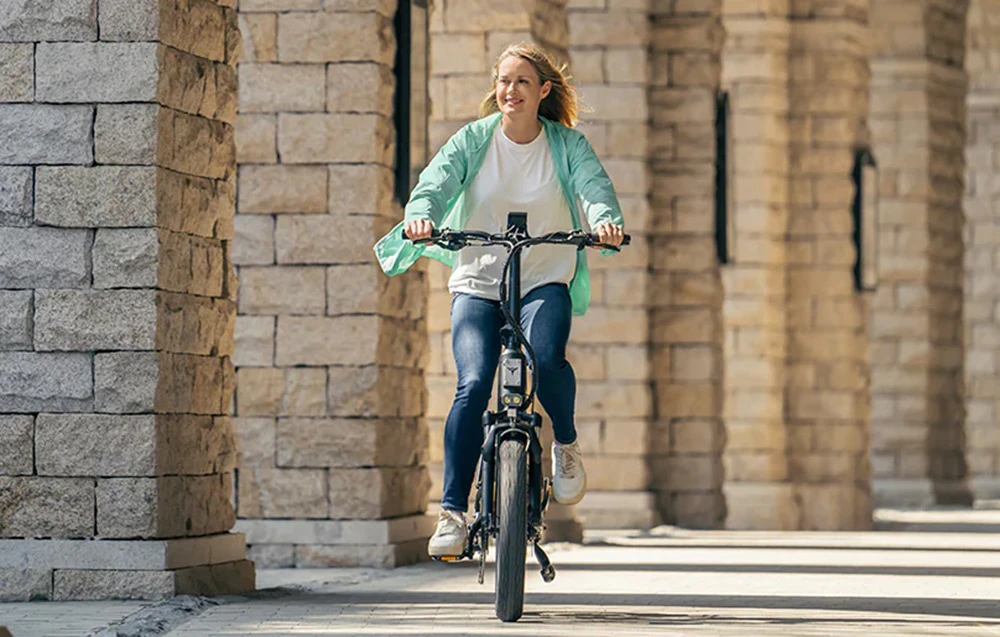 O femeie merge pe o bicicletă electrică între coloane de piatră