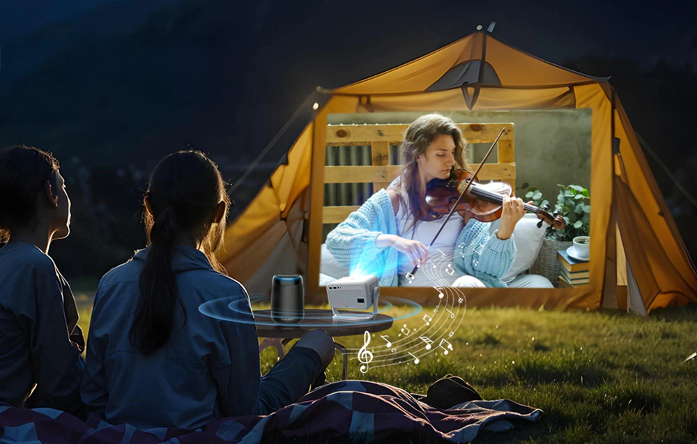 Oameni care vizionează un film proiectat pe peretele unui cort în timpul unei excursii de camping nocturne