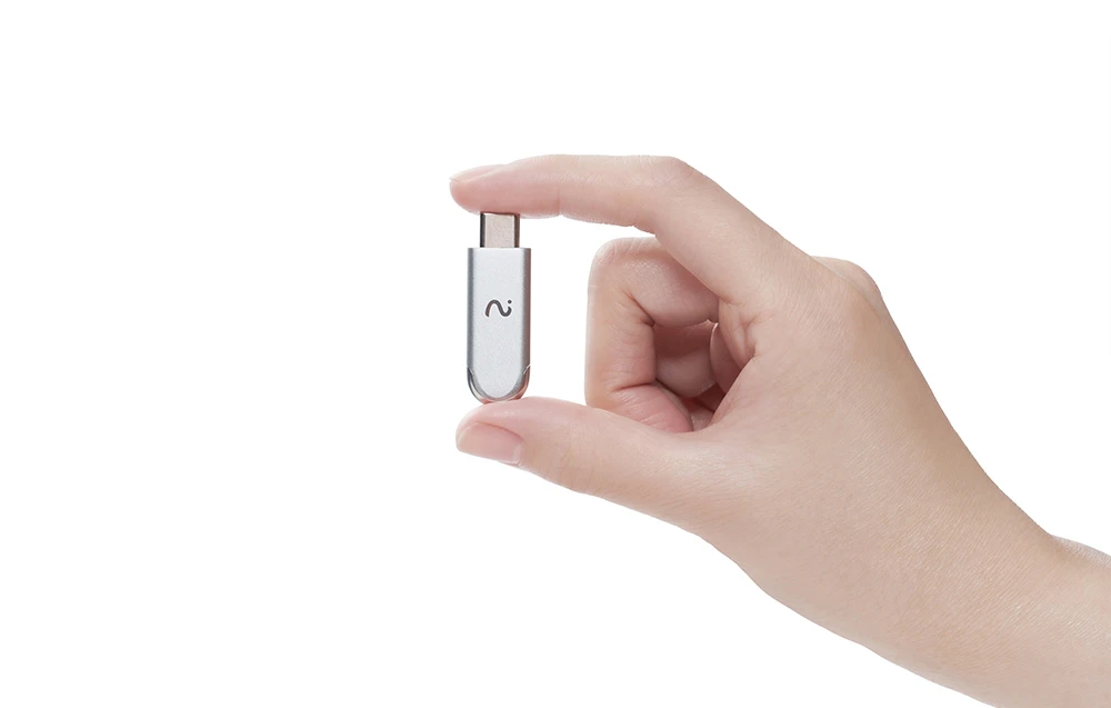 Un dongle metalic cu capete rotunjite, prevăzut cu un simbol în formă de undă și o mică gaură, este ținut între două degete.