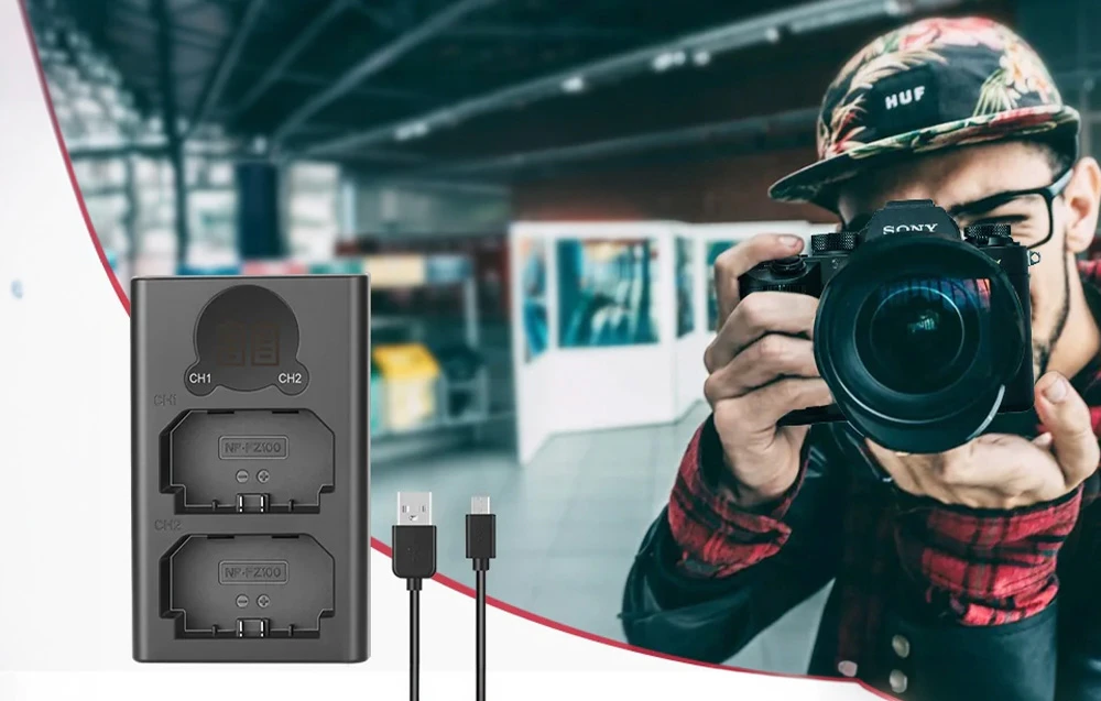 Un încărcător dublu pentru baterii cu un cablu USB lângă un fotograf care face o fotografie cu un aparat foto.
