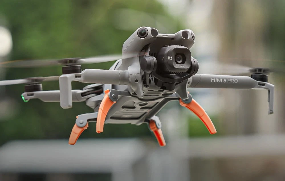 Dronă zburătoare DJI Mini 5 Pro cu picioare desfăcute portocalii, plutind în aer