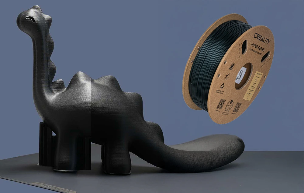 Un model de dinozaur negru imprimat la o imprimantă 3D lângă o bobină de filament Creality Hyper Series