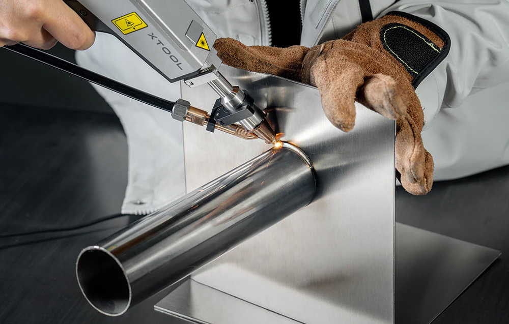 o persoană folosește un aparat de sudură cu laser pentru a prelucra o țeavă metalică