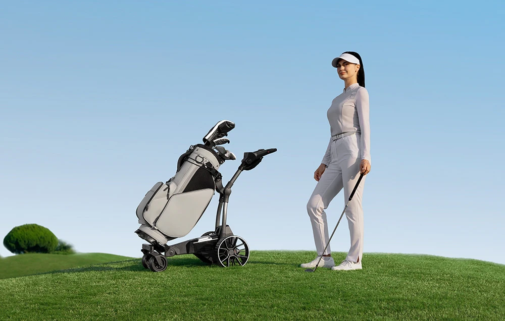 O jucătoare de golf stă cu o crosă lângă o mașinuță de golf automată cu o geantă, pe fundalul unui cer albastru limpede
