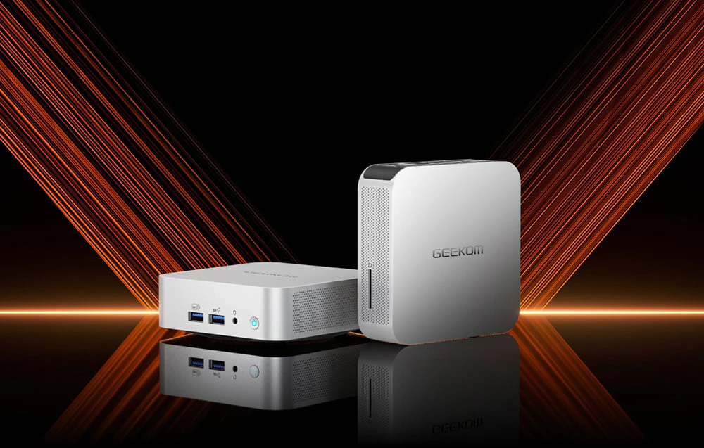 2 mini PC-uri Geekom gri pe o masă de culoare închisă, pe un fundal negru și portocaliu