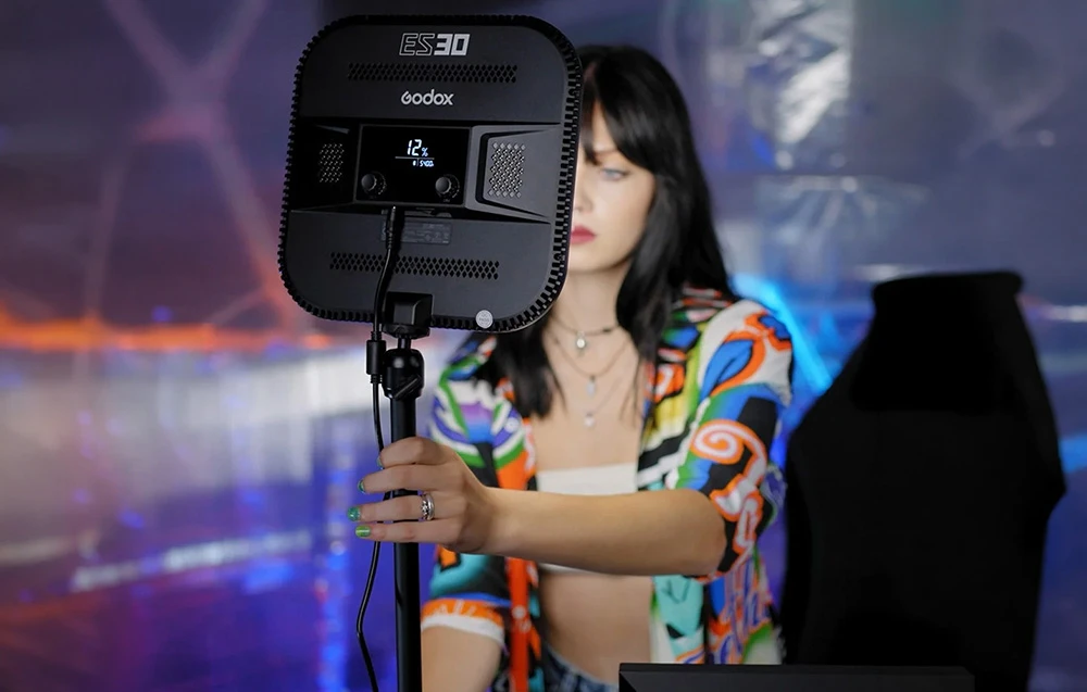 O persoană care ține un trepied, cu partea din spate a lămpii Godox ES30 prevăzută cu un afișaj