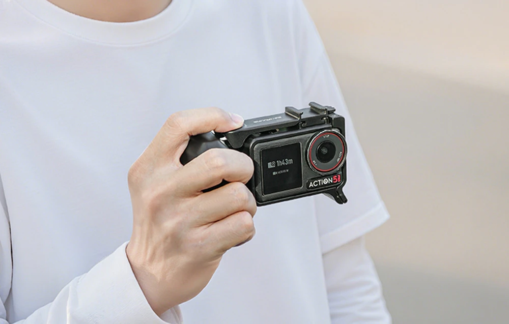 O persoană îmbrăcată într-un tricou alb ține camera Action 5 într-un cadru cu mâner; ecranul afișează „1h43m” și parametrii „4K 60/RS/W”