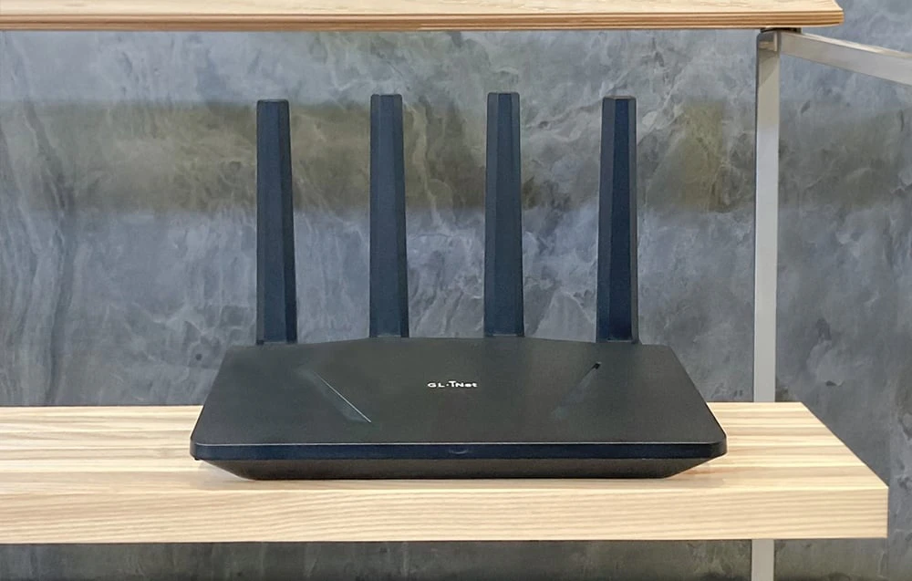 Un router negru cu patru antene verticale, așezat cu fața spre în față pe un raft din lemn de culoare deschisă