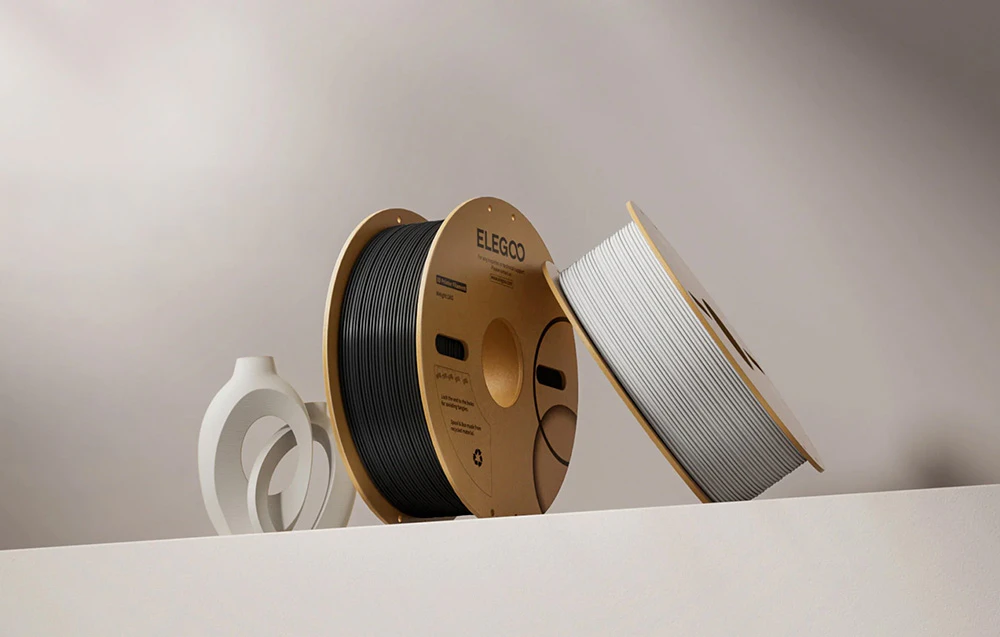 Două bobine de filament Elegoo – alb și negru – cu imprimare decorativă pe fundal
