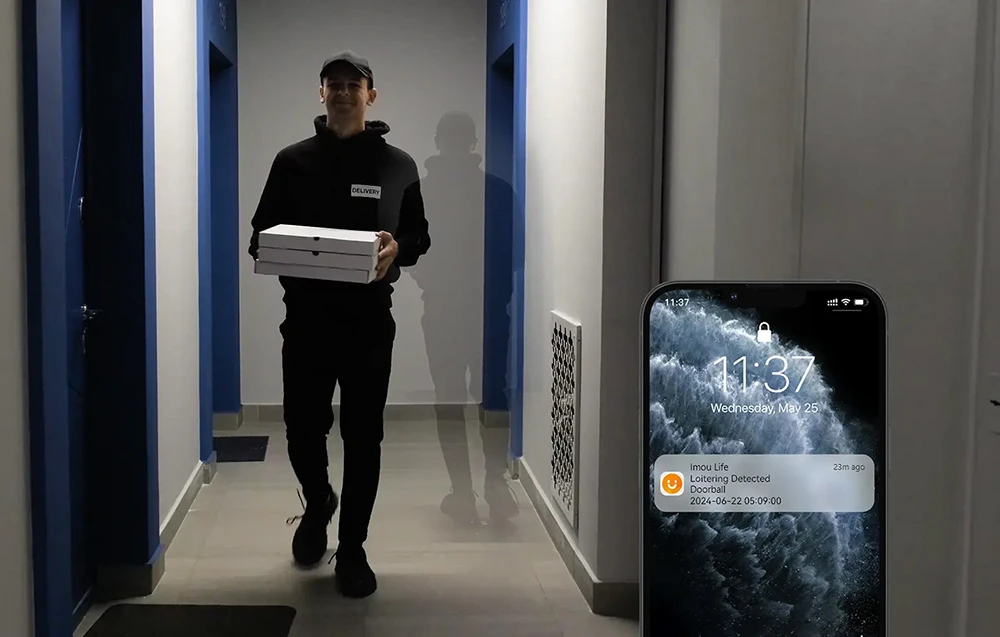 Livrator de pizza în hol; lângă un smartphone cu o notificare Imou Life: Detectare rătăcire, Doorball, 22.06.2024