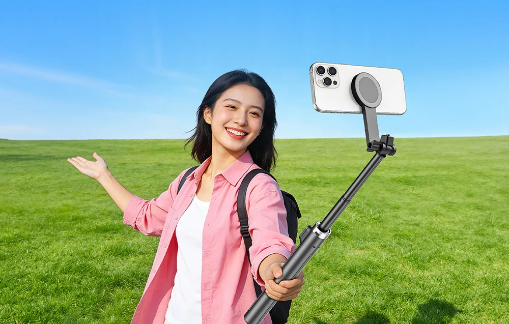 O femeie într-o poiană verde, ținând un gimbal Aochuan cu un smartphone montat pe un conector magnetic