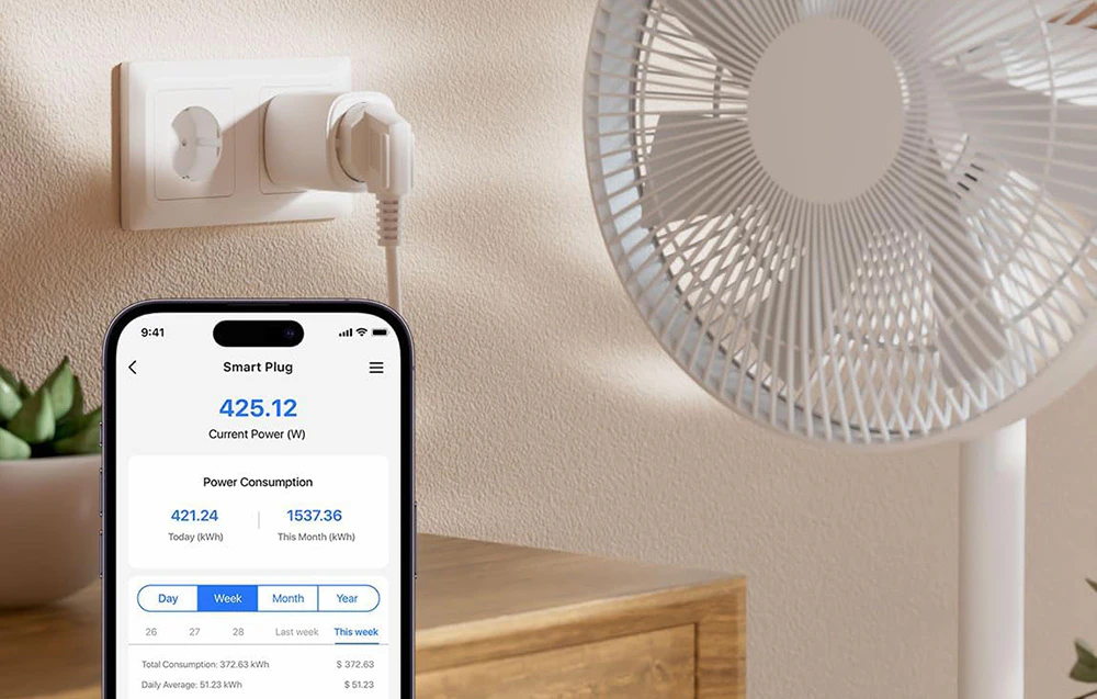 Smartphone care afișează o aplicație pentru monitorizarea consumului de energie al unei prize inteligente conectate la un ventilator așezat pe o comodă din lemn