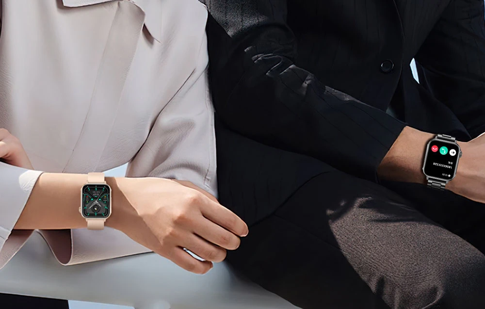 O femeie în haină albă și un bărbat în haină neagră stau cu smartwatch-uri la încheieturi.