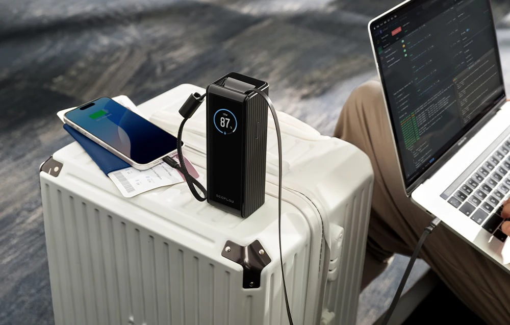 Un powerbank cu afișaj se află pe o carcasă conectată la un smartphone și un laptop.