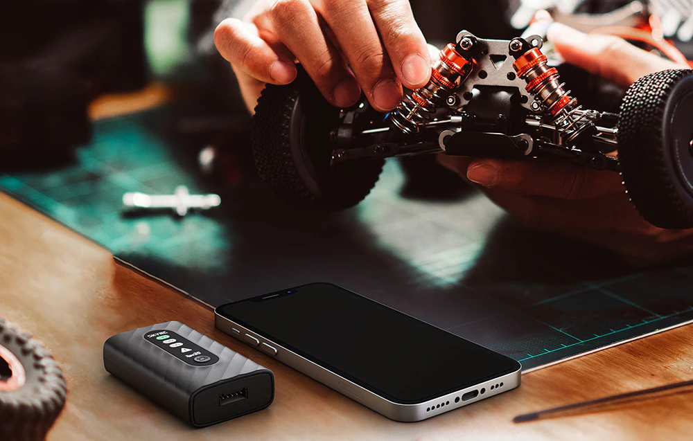 Încărcător SkyRC Type35 pe un birou lângă un smartphone în timp ce se lucrează la un model RC.