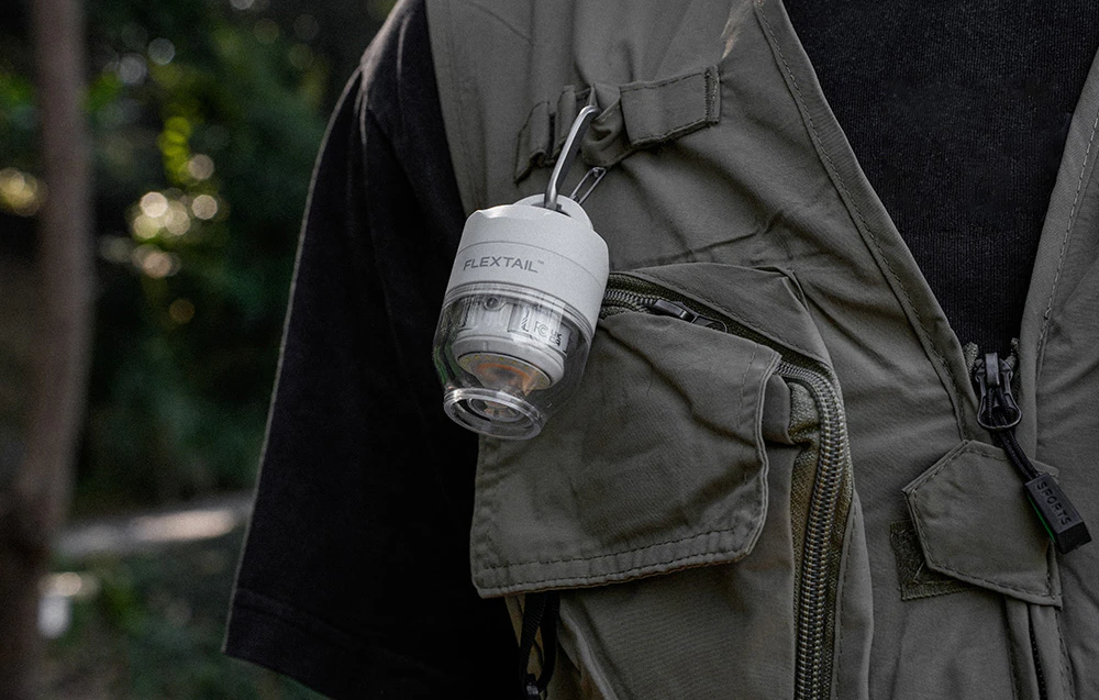 O mică pompă Flextail albă este atașată cu un carabinier la bucla unei veste de drumeție verde-măsliniu