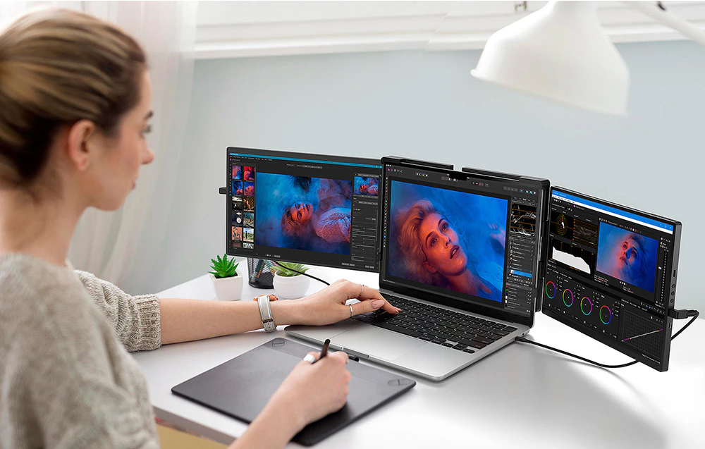 Femeie la birou editând o fotografie portret pe un laptop cu două ecrane suplimentare și o tabletă grafică
