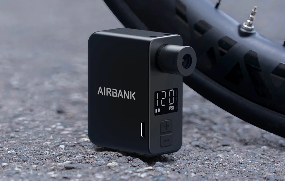 O pompă portabilă de bicicletă cu afișaj digital așezată pe asfalt lângă o roată de bicicletă.