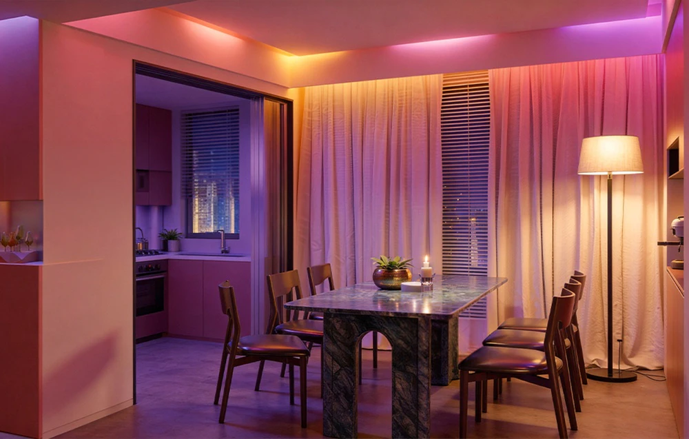 Sufragerie cu o masă mare, de culoare închisă, și scaune, iluminată de o lampă și o bandă LED colorată