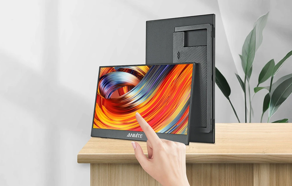 O femeie atinge ecranul unui monitor portabil cu grafică colorată, așezat pe o masă de lemn.