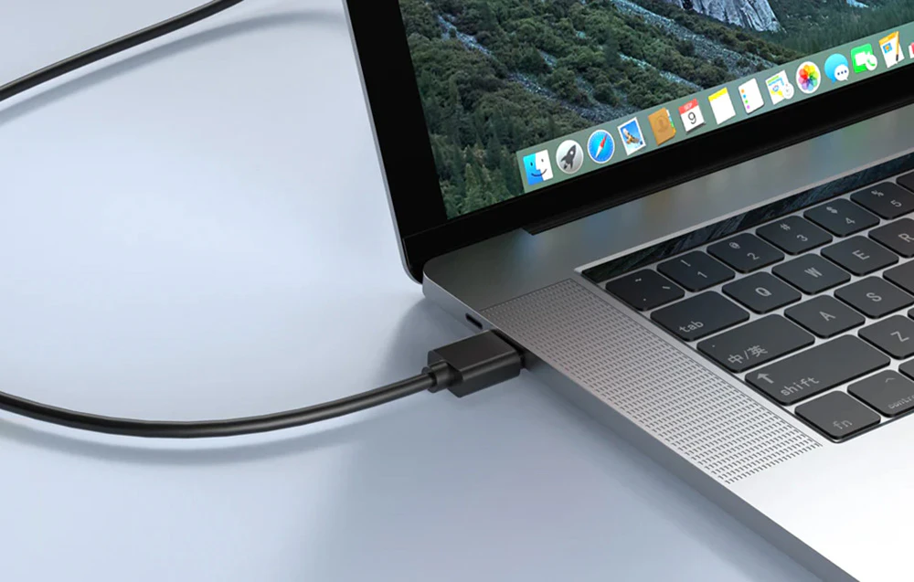 Un prim-plan al unui cablu negru conectat la un port de pe partea laterală a unui laptop argintiu.