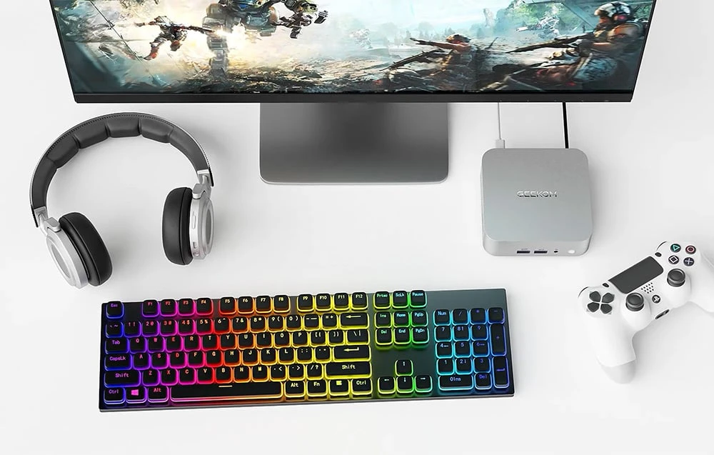 Mini PC Geekom pe un birou lângă o tastatură, un monitor, căști și un gamepad