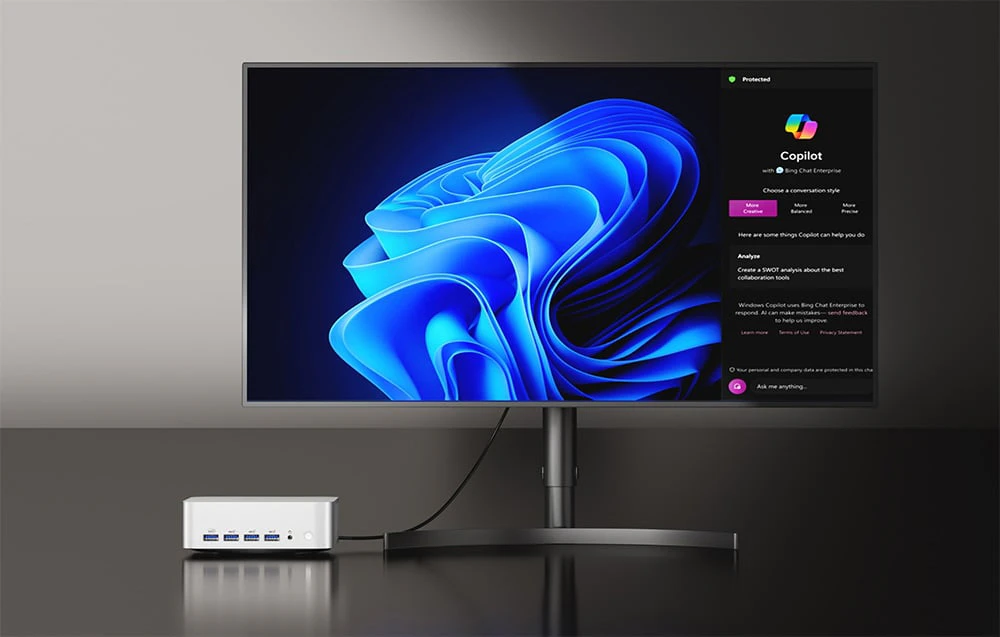 un mini PC Geekom alb conectat la un monitor care afișează grafică abstractă