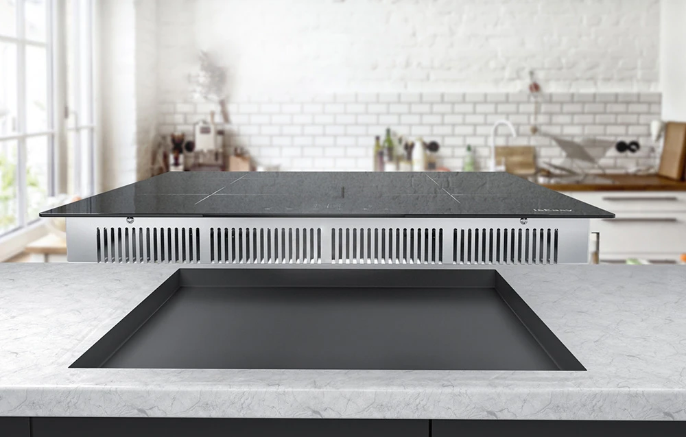 Plită cu inducție cu sistem de ventilație vizibil deasupra blatului încastrat într-o bucătărie luminoasă