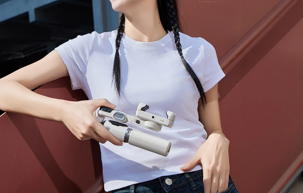 O femeie îmbrăcată într-un tricou alb ține în mâini un gimbal pliat, în fața unui perete roșu.