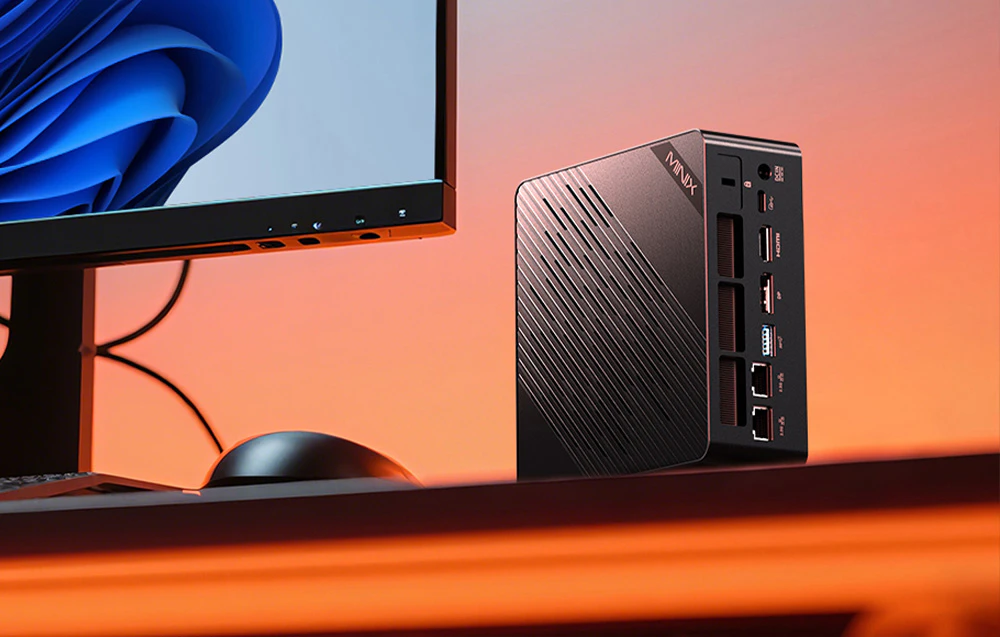 Mini PC MINIX plasat vertical pe un birou, lângă un monitor, cu porturile vizibile pe partea din spate a carcasei.