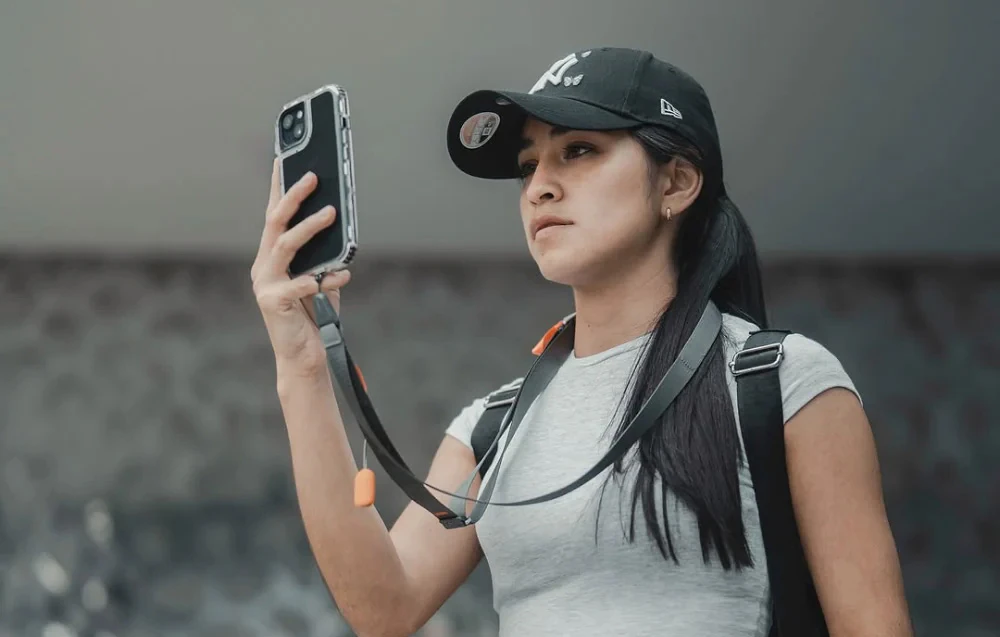 O femeie purtând o șapcă de baseball care își utilizează telefonul, care este montat pe o curea de gât