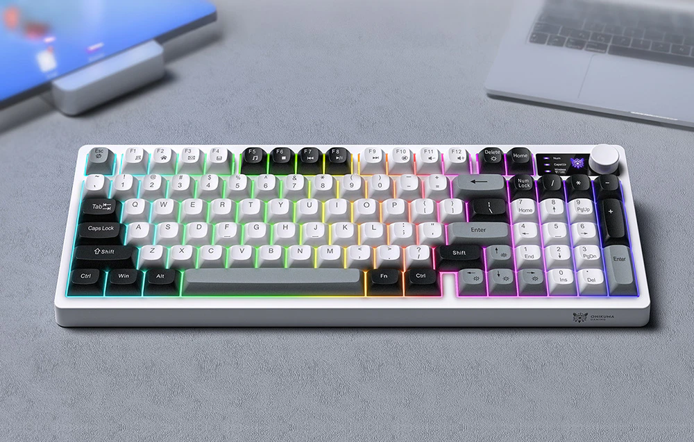 O tastatură cu iluminare colorată așezată pe un birou gri, lângă o tabletă și un laptop