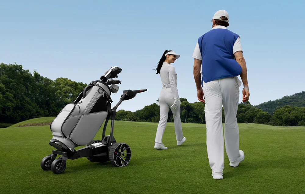 Doi jucători de golf traversează terenul de golf lângă o mașinuță automată cu o geantă de golf