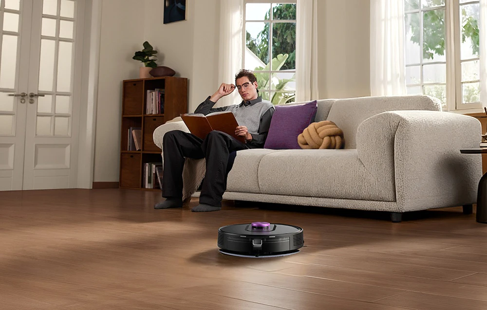 Robotul aspirator W15 curățând într-un living unde un bărbat citește o carte